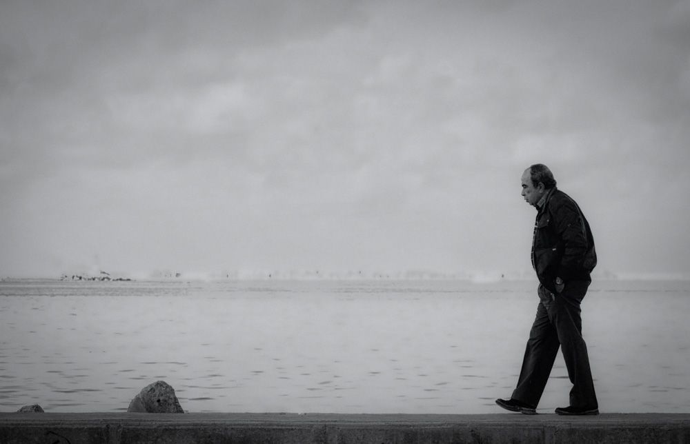 Older man walking alone by the water's edge