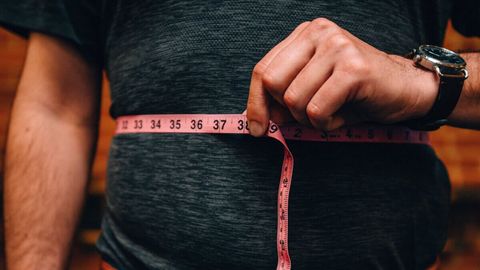 Close up of a man holding measuring tape around his waist 