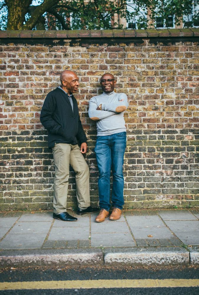 Two Black men leaning against a wall and talking.