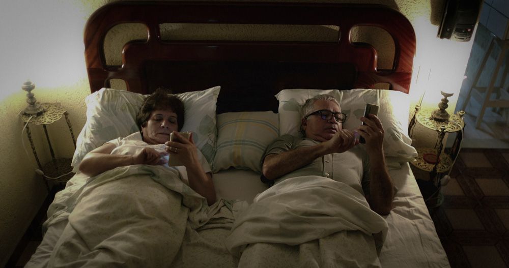 Older man and female partner in bed looking at their phones