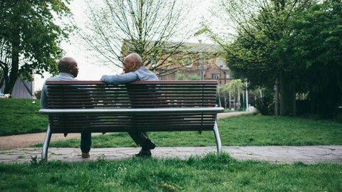 Two Black men chatting on a park bench 
