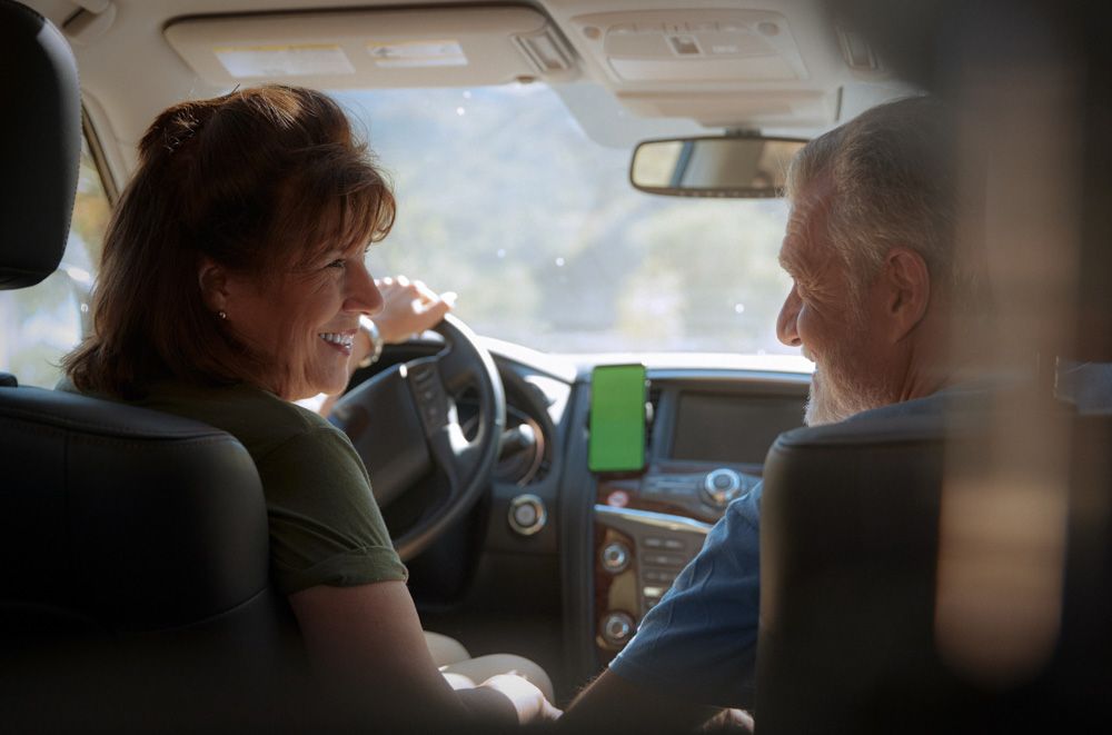 Older woman behind the wheel of a car smiling at the male passenger