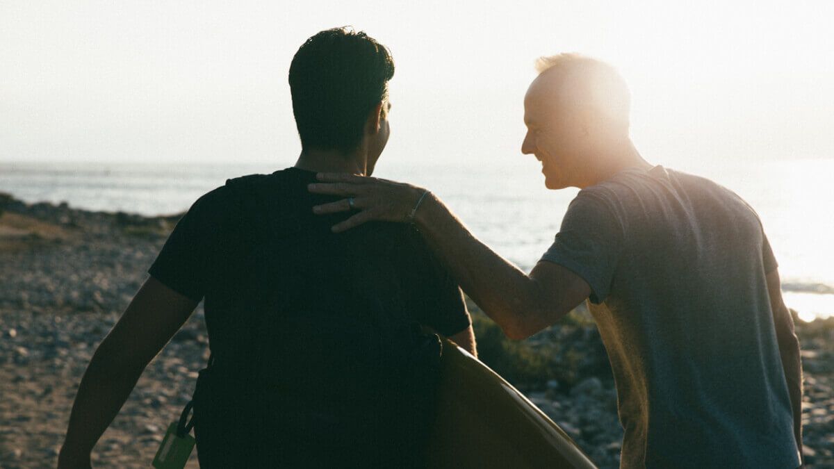 Two men walking towards beach with surfboard.