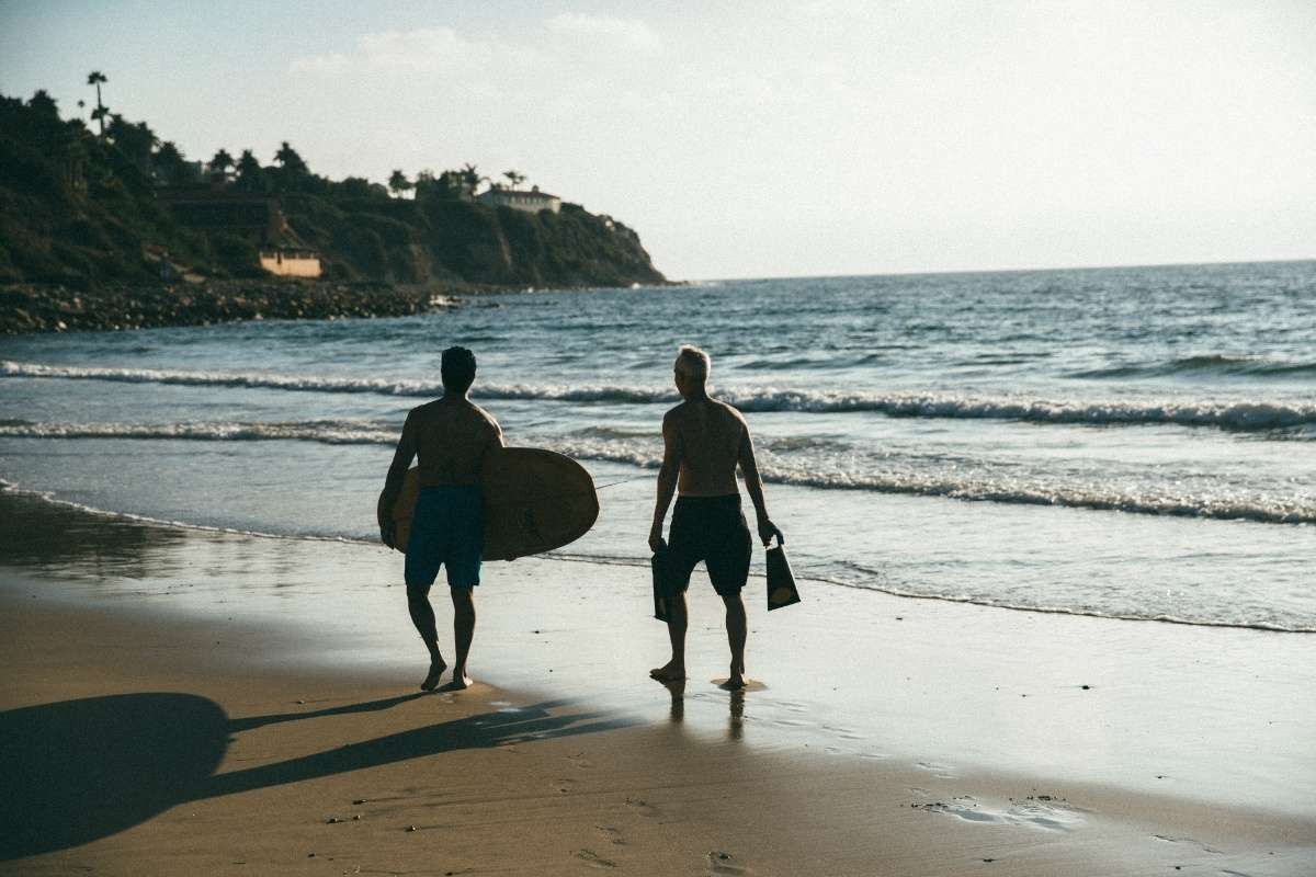 Two men with a surfboard walking towards beach